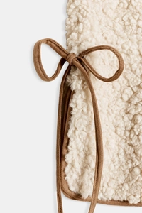 Detail of cream sherpa vest featuring a brown faux suede side tie-knot bow closure