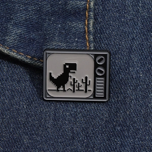 Detail of pixel art dinosaur enamel pin styled as an old TV on dark denim fabric