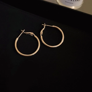 Macro shot of gold geometric hoop earrings on black velvet with glossy metal finish
