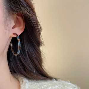 Close-up of tortoise shell resin hoop earrings worn by a model in warm lighting