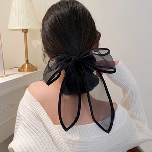 Détail d'une grande pince à cheveux avec nœud en tulle noir portée sur un chignon bas