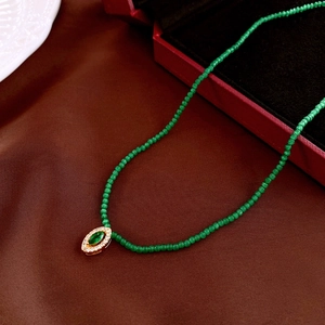 Detailed shot of emerald green beaded necklace with oval gold pendant and white zircons