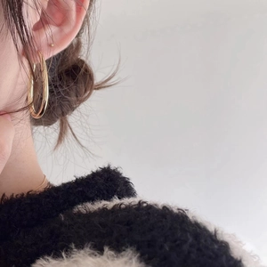 Close-up of a model wearing large polished gold hoop earrings in a minimalist style