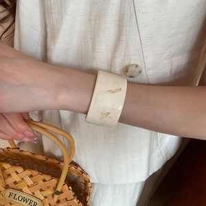 Close-up of wide cream marble resin bangle with elegant amber fluid texture on wrist