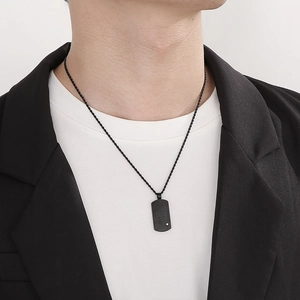 Gros plan d'un pendentif plaque noire avec gravure et petit diamant sur chaîne torsadée