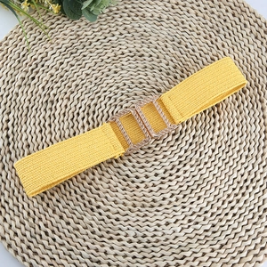 Detail of yellow elastic woven belt with a square interlocking gold metal buckle on straw mat