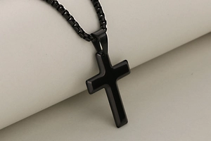 Gros plan d'un pendentif croix en acier inoxydable noir poli avec sa chaîne maille vénitienne