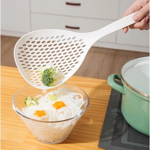 White stainless steel noodle strainer lifting broccoli from a bowl of pasta noodles