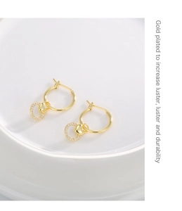 Detail of gold heart earrings with cubic zirconia on white ceramic background