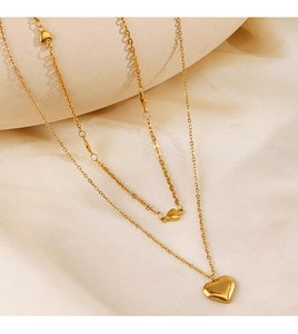 Détail d'un collier doré à double rangée avec deux pendentifs en cœur sur tissu doux
