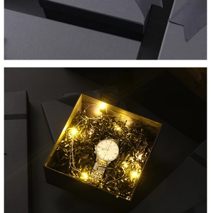 Detail of square black gift box with ribbon, interior raffia, and warm LED light string