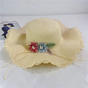Detail of beige straw hat with red and blue fabric flowers and scalloped lace brim