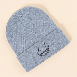 Close-up of light blue knitted beanie featuring black embroidered cross-eyed smile design