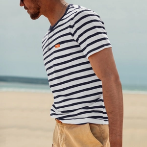 Detail of men's blue and white striped T-shirt with orange logo on a beach background