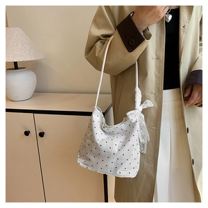 Close-up of white polka dot bucket bag featuring a lace bow on the shoulder strap