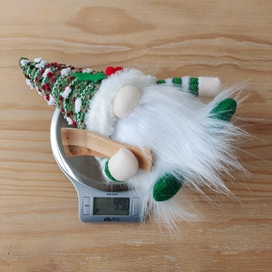 Close-up of a green knitted Christmas gnome on a scale weighing 99 grams
