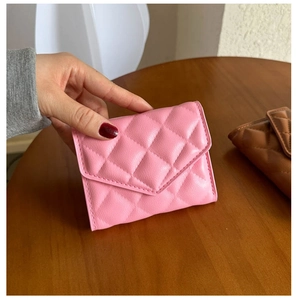 Close-up of pink quilted faux leather folding wallet being held over a wooden surface
