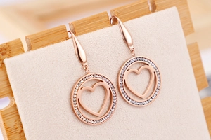 Close-up of rose gold hollow heart earrings with paved crystals on a beige display