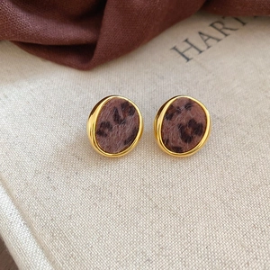 Detail of round leopard print plush earrings with gold metal frame on a beige book