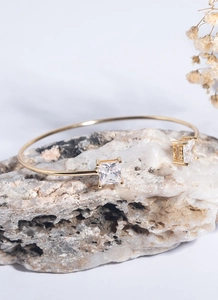 Detailed shot of gold open bangle with square cubic zirconia on a natural stone base