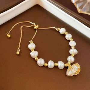 Détail d'un bracelet en perles d'eau douce avec un pendentif coquillage doré et cristaux