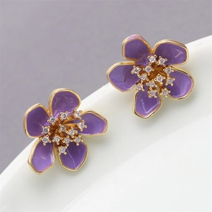 Close-up of purple flower stud earrings with gold trim and sparkling crystals