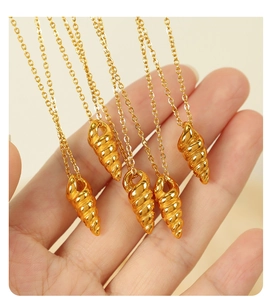 Close-up of a gold conch pendant necklace held in hand showing delicate spiral detail