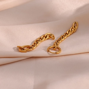 Gros plan de boucles d'oreilles chaîne Figaro dorées sur un tissu satiné rose doux