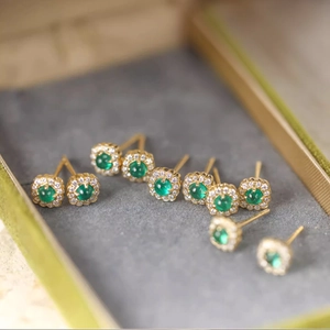 Macro shot of gold emerald stud earrings with green center stone and halo diamonds