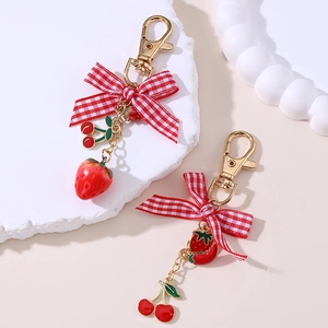Detail of red cherry and strawberry keychains with checkered bows on a white stone base