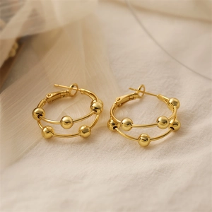 Close-up of gold-plated double hoop earrings with metal beads on soft fabric