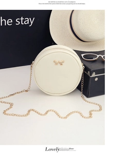 Detail of round white crossbody bag with gold chain strap and metallic bow decoration