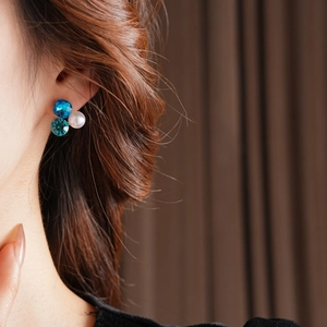 Macro shot of triangle stud earrings featuring blue crystals and a round white pearl