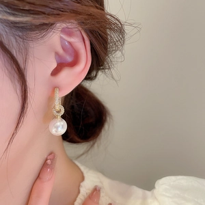 Détail d'une boucle d'oreille dorée avec micro-pavage de zircone et perle blanche pendante