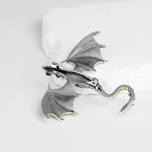 Vintage silver dragon brooch with green enamel wings on white stone background