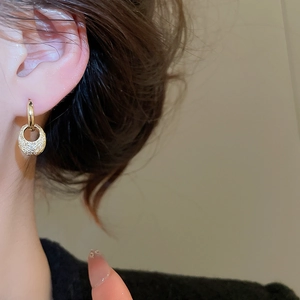 Close-up of golden oval textured dangle earrings on a model with a minimalist aesthetic