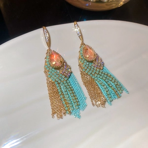 Close-up of teardrop pink gemstone earrings with mint beads and gold chain tassels