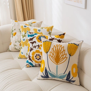 Detail view of four square pillow covers with yellow floral towel embroidery on beige fabric