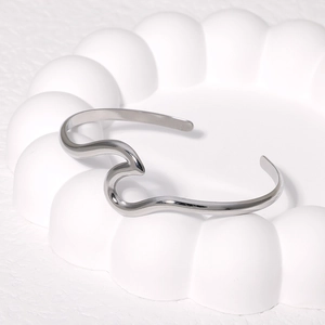 Minimalist silver wavy open cuff bracelet in titanium steel on white textured display