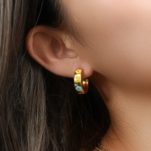Macro detail of gold-plated hoop earrings with colorful enamel floral patterns on ear