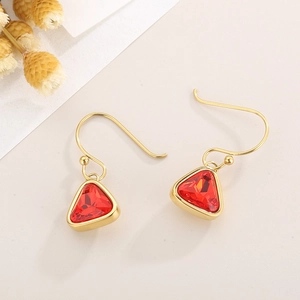 Detail of gold triangle earrings with red crystal stone on beige background
