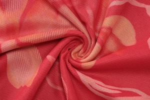 Gros plan sur tissu en maille rouge avec imprimés orange et rose montrant texture et drapé