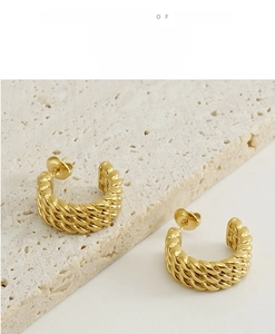 Detailed view of gold twisted C-shape hoop earrings on a minimalist stone display pedestal