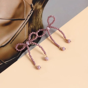 Detail of handmade beaded bow earrings in mauve purple with elegant pearl accents