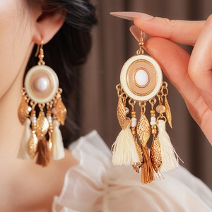 Macro detail of bohemian tassel earrings featuring white gemstones and leaf charms