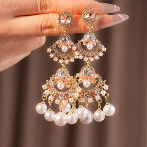 Detailed shot of fan-shaped fringe earrings with pink gems and white pearls on gold base