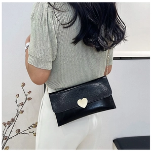 Detail of black leather clutch bag with golden heart buckle and elegant chain strap