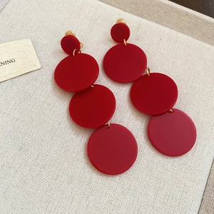 Macro view of long vibrant red four-tier acrylic drop earrings on a textured fabric