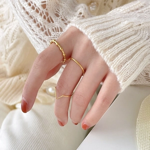 Close-up of three minimalist gold rings including beaded and V-shape styles worn on a hand