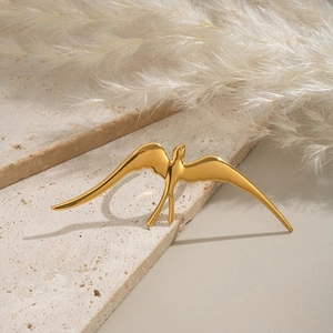 Artistic close-up of golden swallow bird ring on beige travertine stone with feathers
